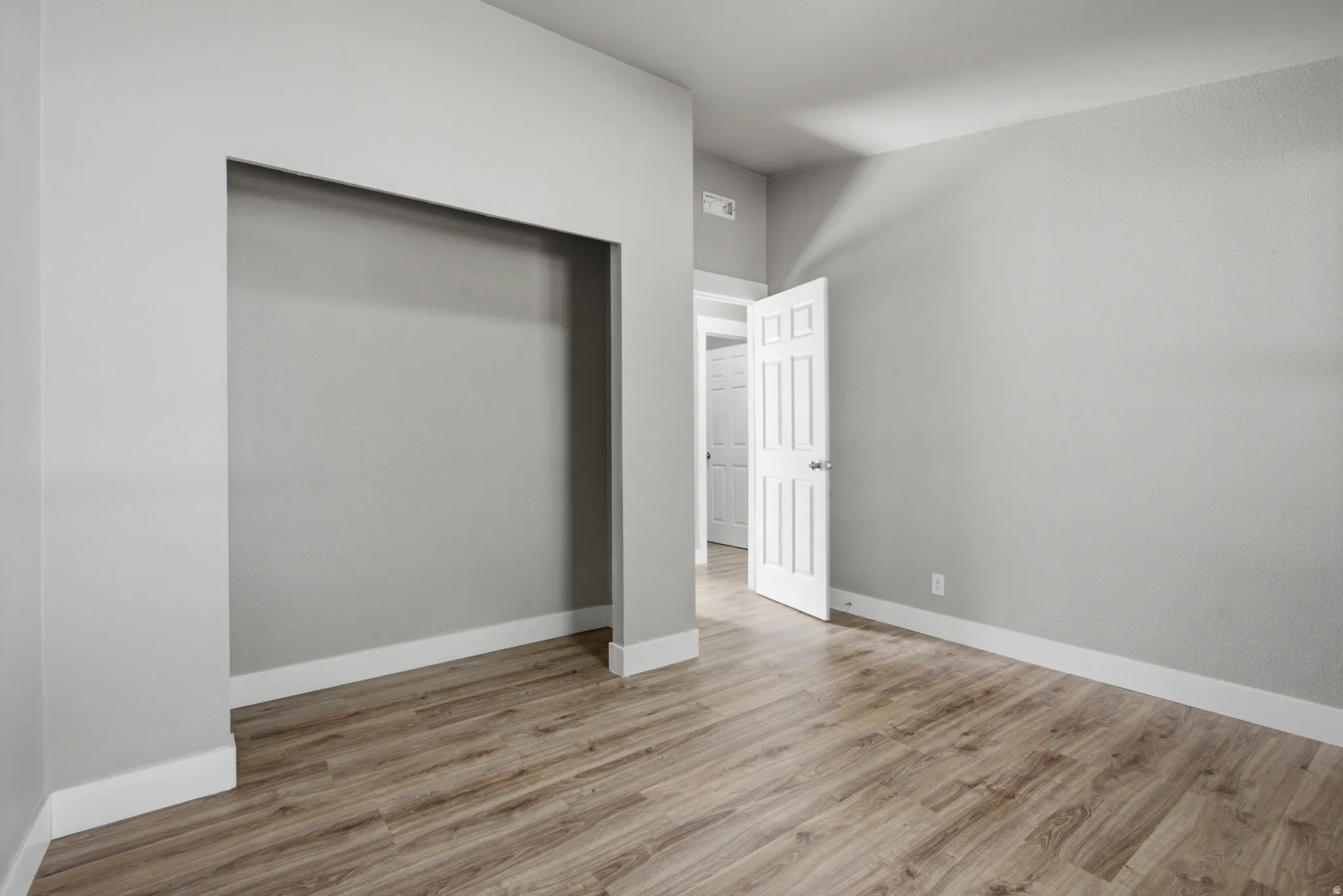 Recessed wall space, wood-finish flooring, white trim, and a paneled door