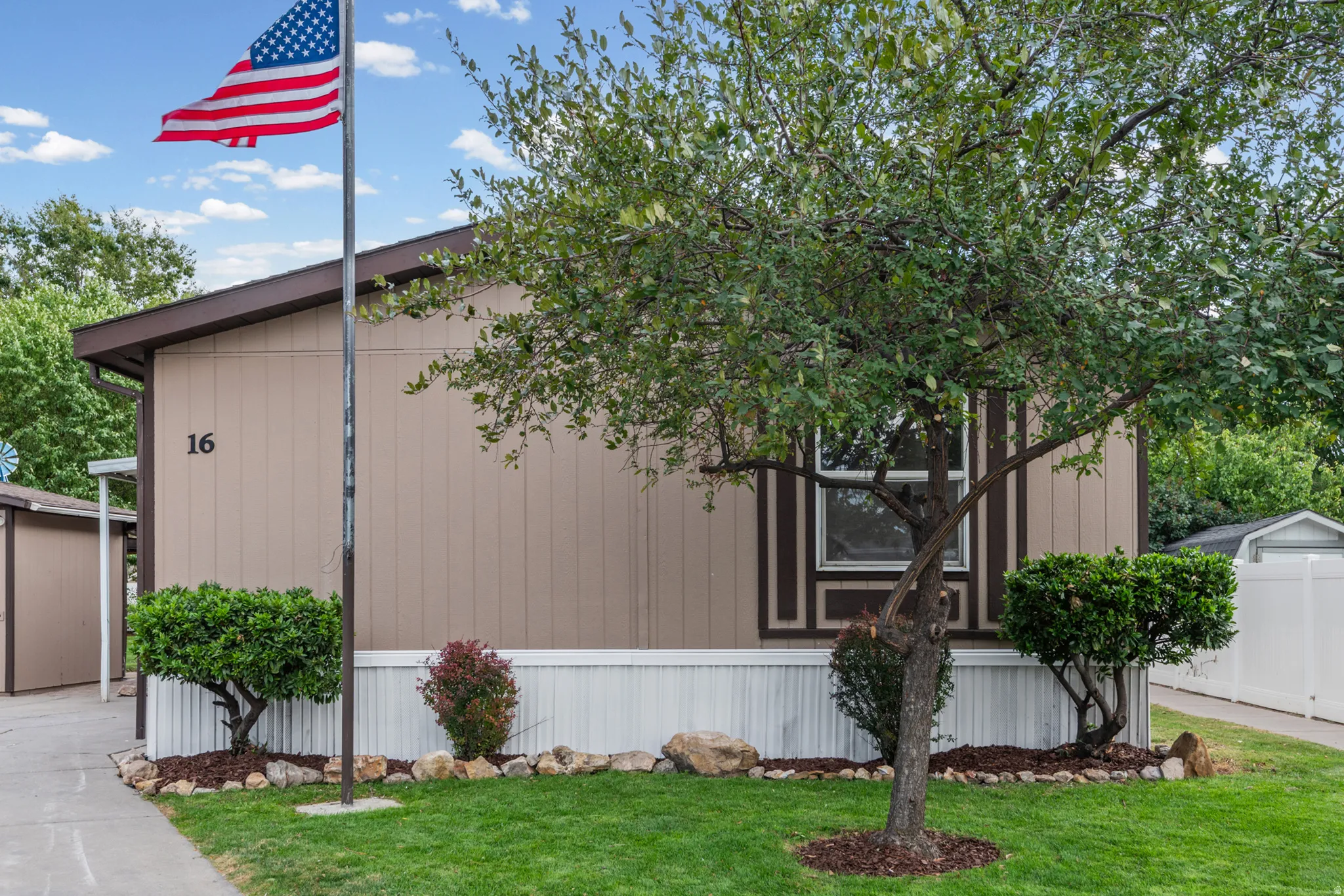 Manicured lawn with a mature tree, stone-lined landscaping beds with mulch and shrubs, and a side building