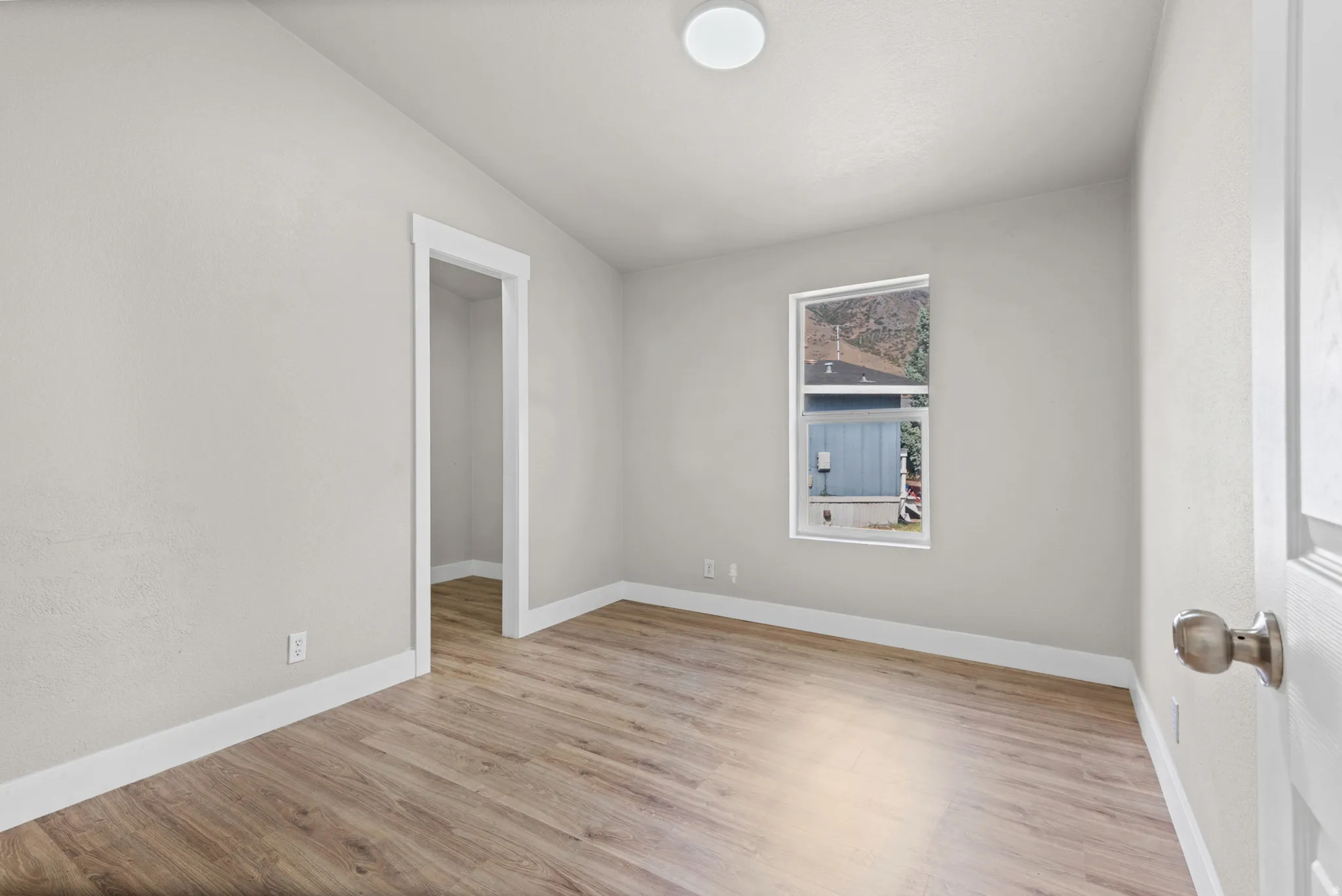 Light-toned walls, wood-finish flooring, white trim, recessed lighting, and a window