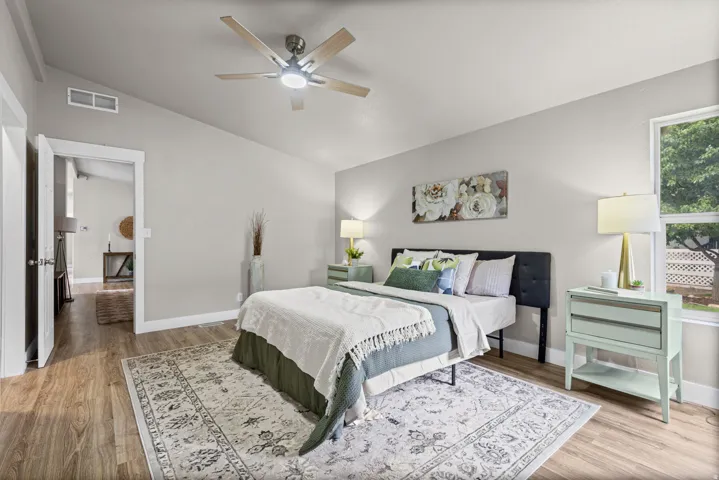 Wood-finish flooring, vaulted ceiling, ceiling fan with integrated lighting, window with exterior lattice, and neutral wall tones