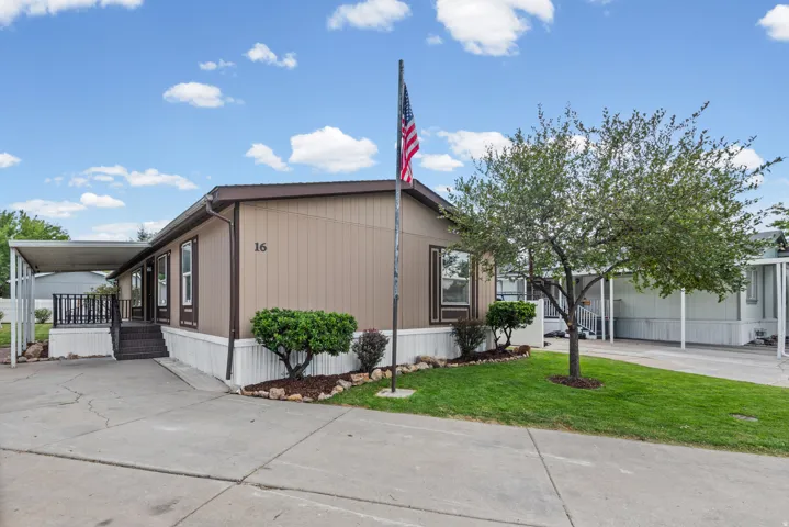 Charming manufactured home featuring a metal exterior with neutral earth-tone siding, covered front porch with railing, and an American flag display