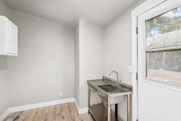 Stainless steel utility sink with a gooseneck faucet, white wall cabinetry, and wood-finish flooring