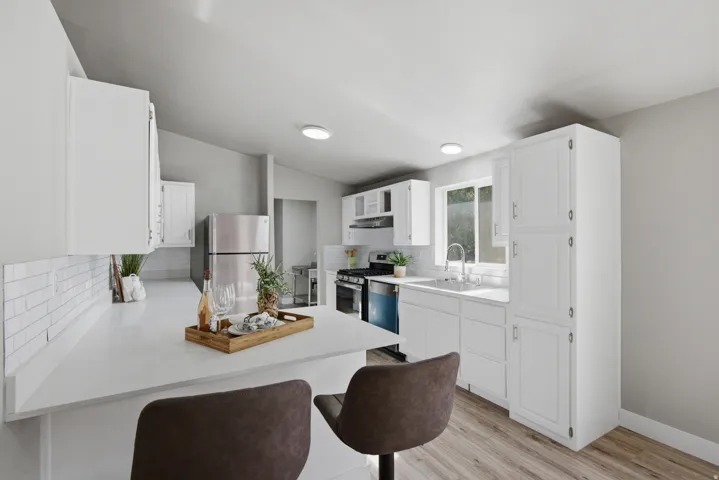 White shaker cabinetry, light-toned wood-finish flooring, white subway tile backsplash, stainless steel appliances, and recessed lighting