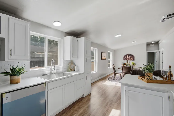 White shaker cabinetry, stainless steel dishwasher, wood-finish flooring, recessed lighting, and a subway tile backsplash