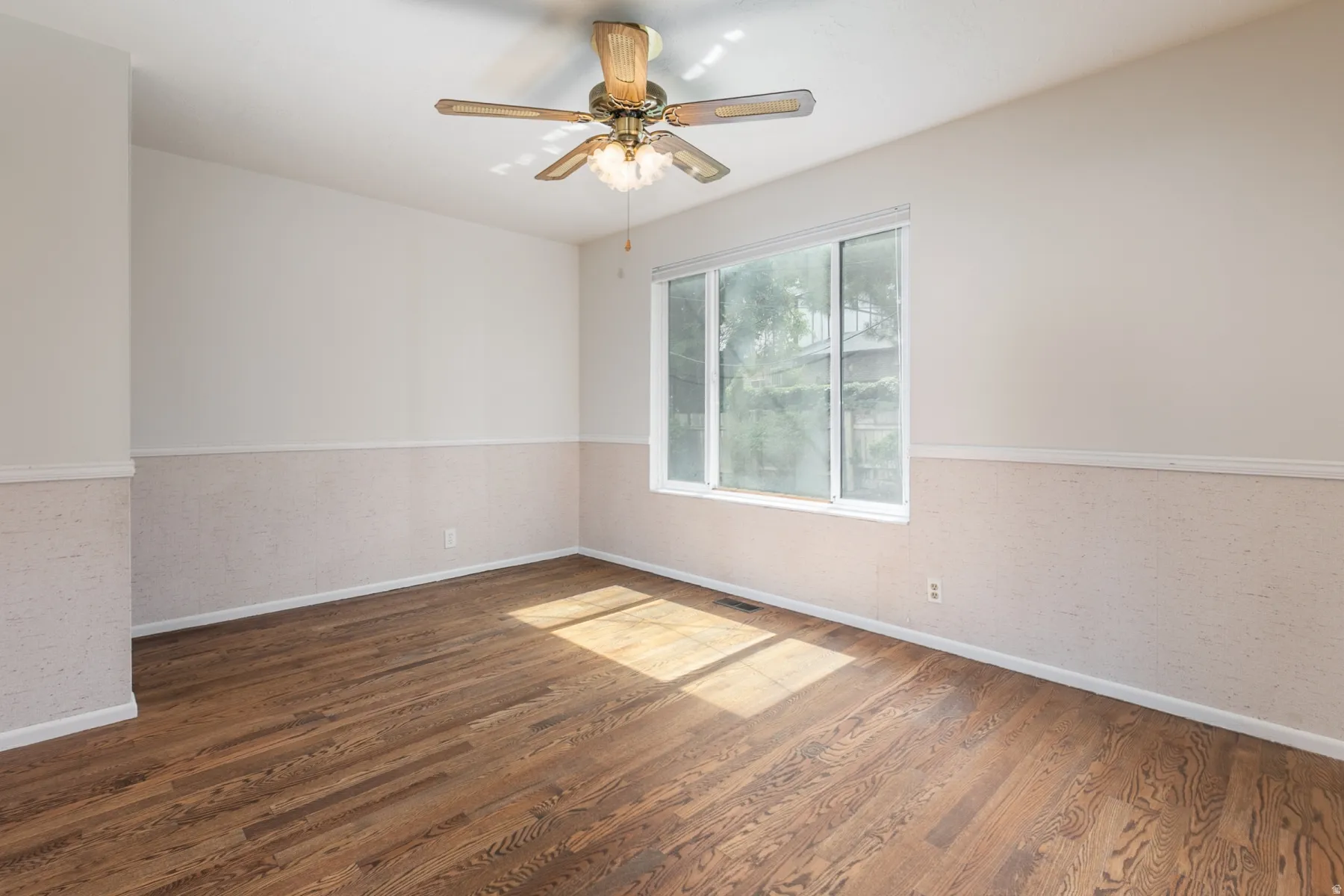 Rich wood-finish flooring, a contemporary ceiling fan, and a large window providing ambient light