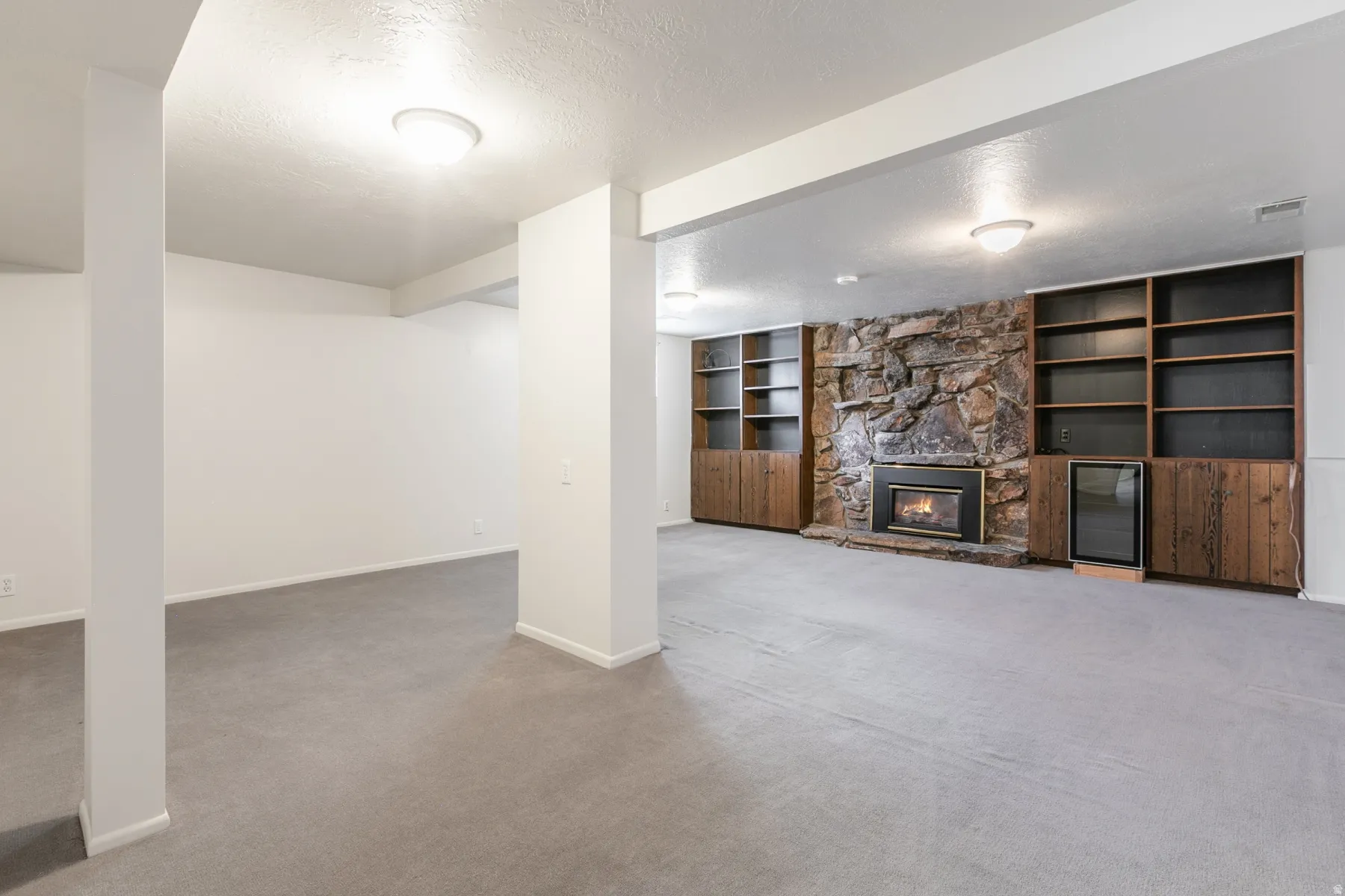 Stone-clad fireplace with black metal insert, built-in shelving, wood-finish cabinetry, and recessed lighting