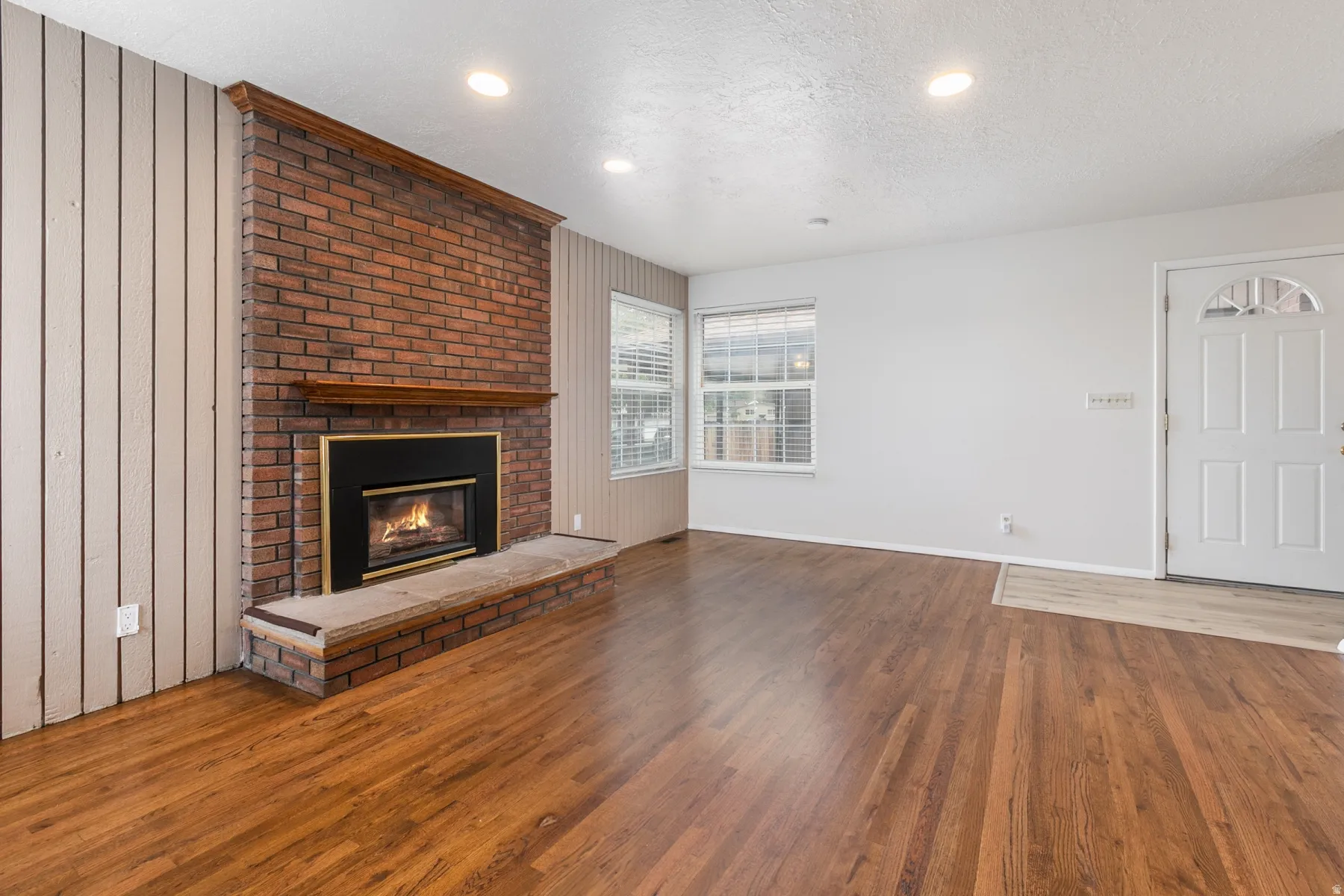 Brick fireplace with wood mantel, built-in hearth, wood-finish flooring, recessed lighting, and a paneled entry door