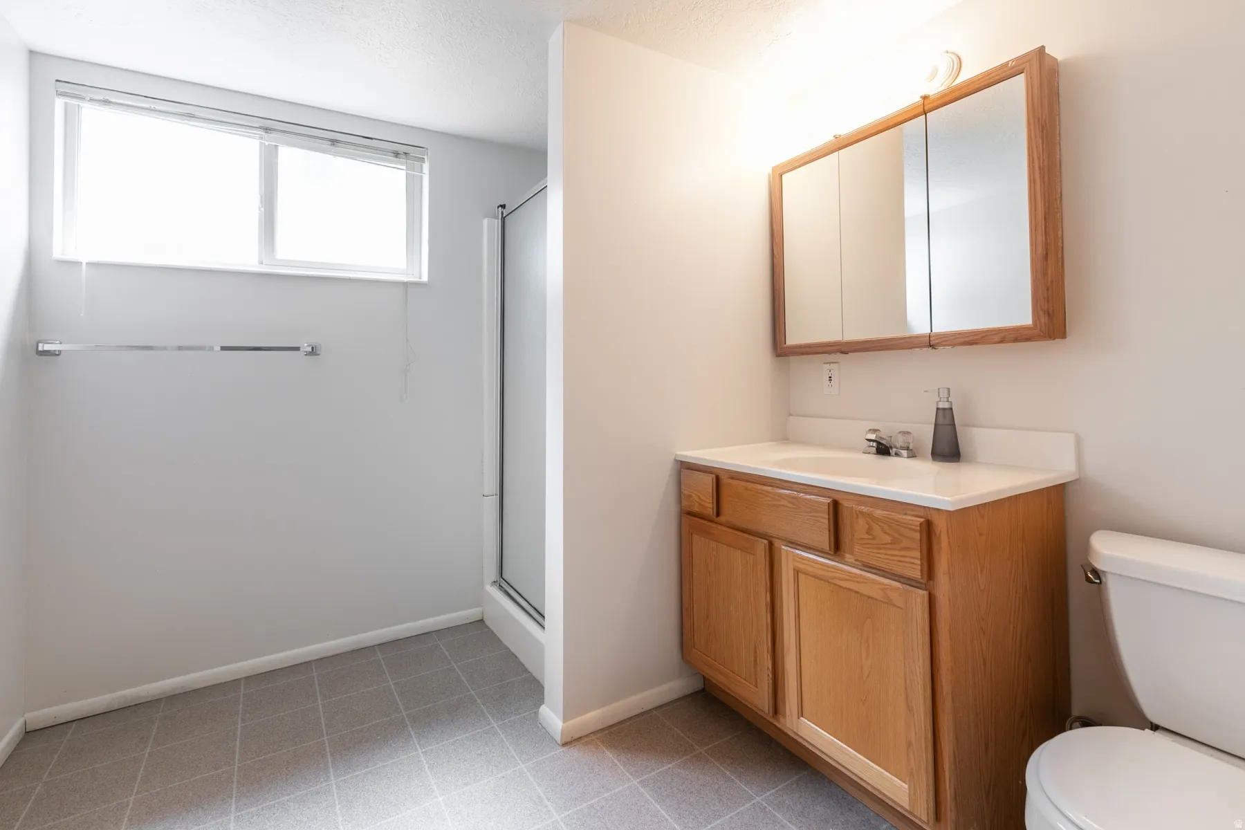 Bathroom with tile flooring, vanity with wood cabinetry, integrated sink, mirrored medicine cabinet, and shower enclosure