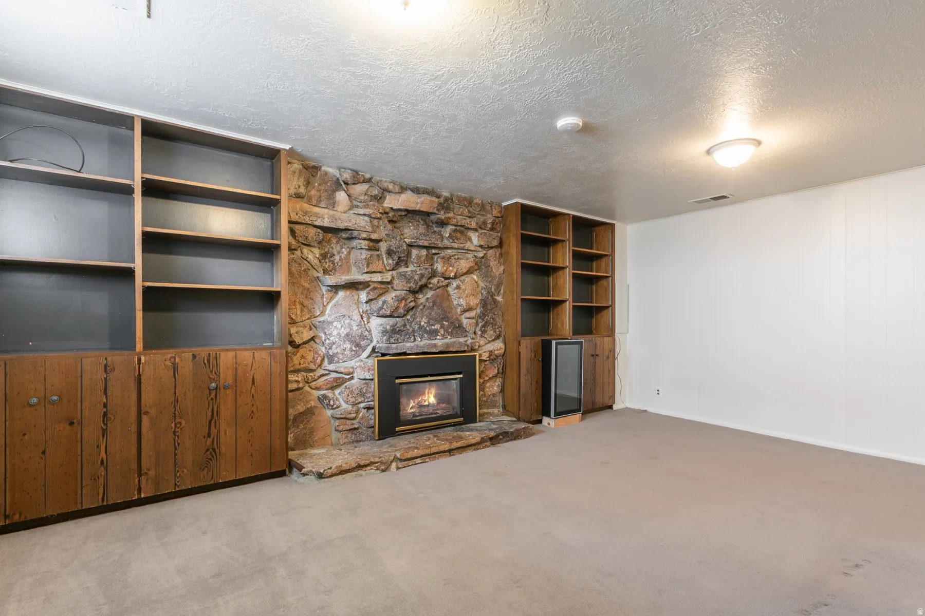 Spacious recreation room featuring custom wood cabinetry with lower storage, open shelving, and built-in stone fireplace with gas insert