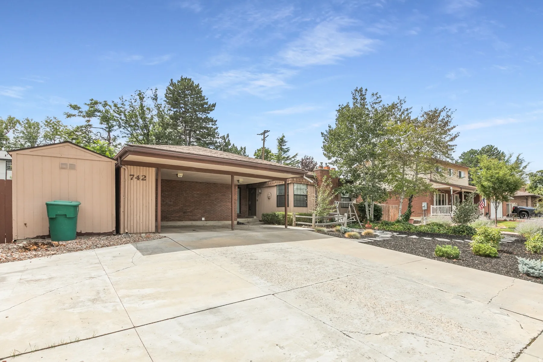 Carport structure with a brick accent wall, dedicated storage shed, and mature landscaping