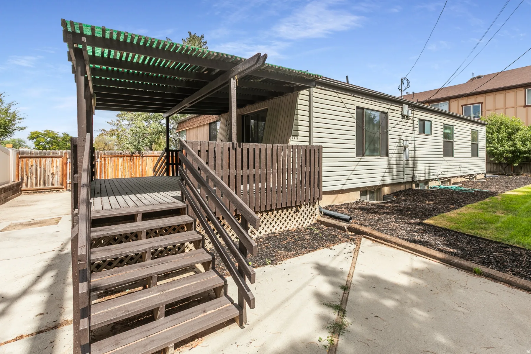 Wood deck with pergola, privacy fencing, and a manicured lawn