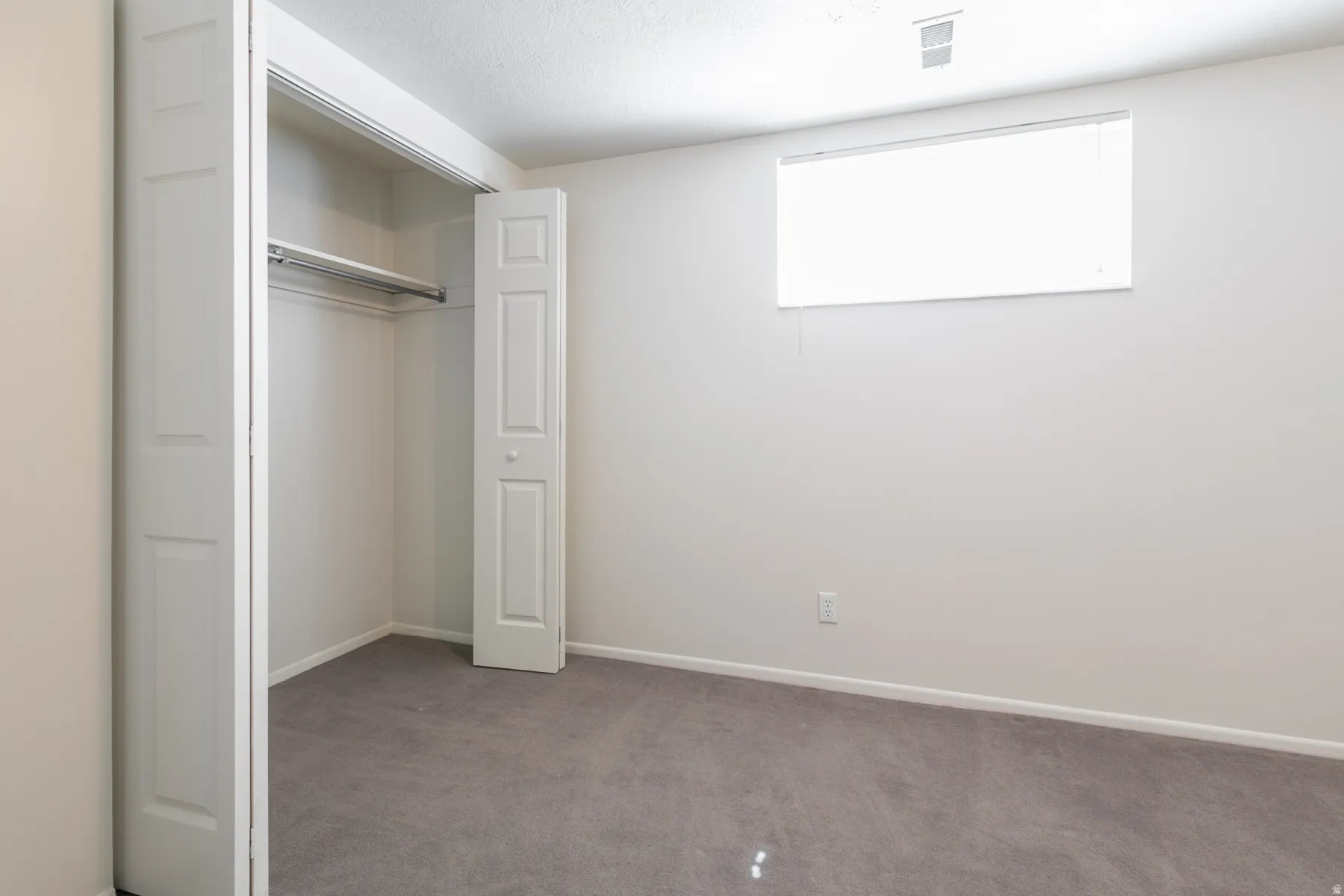 Room featuring a window, gray carpeting, and a bi-fold door closet with a hanging rod