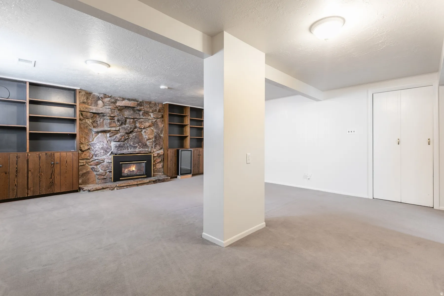 Stone-clad fireplace with a built-in firebox, flanked by custom wood cabinetry with open shelving, light gray carpet, and white walls