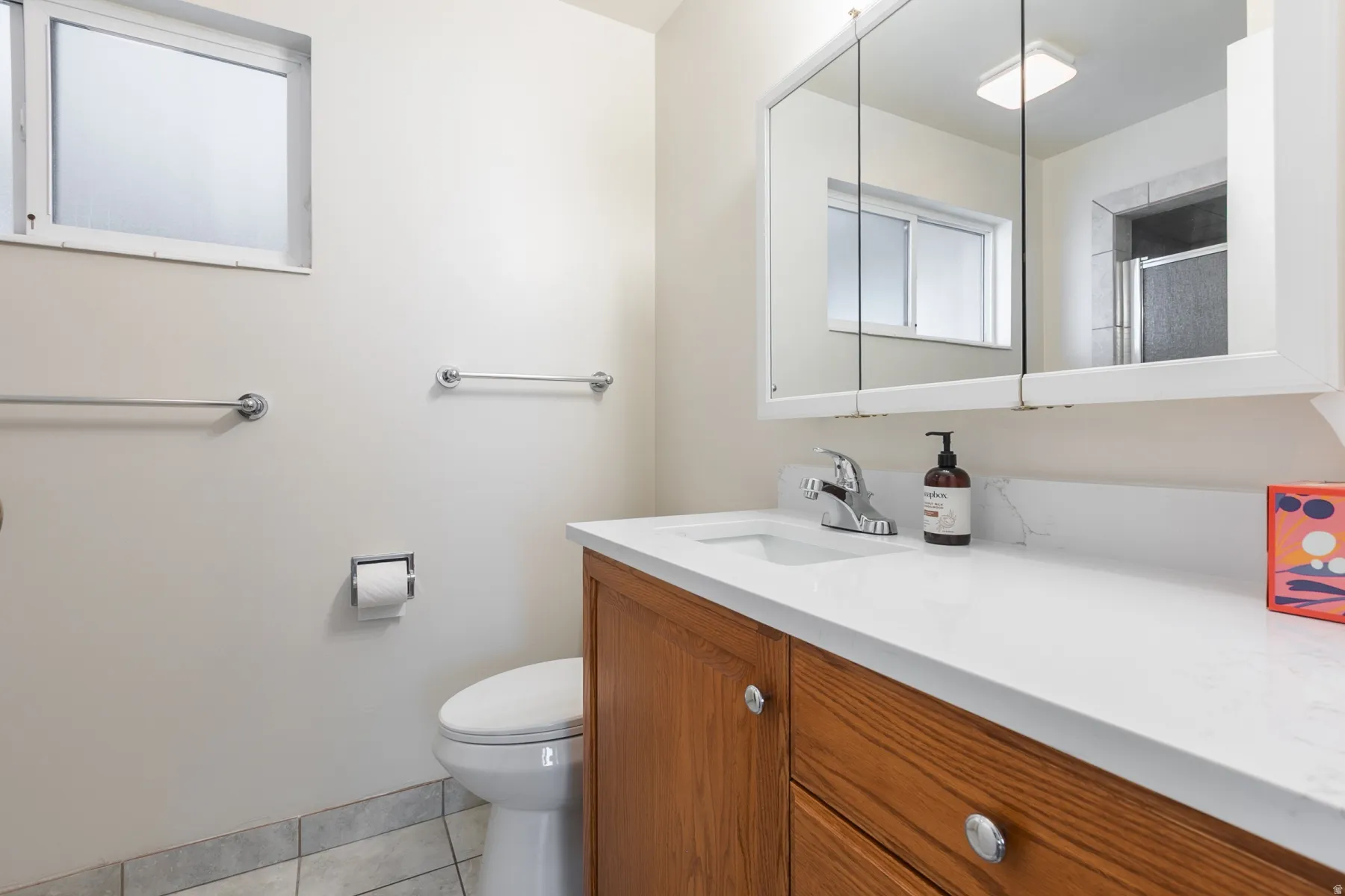 Bathroom featuring a wood-finish vanity with an integrated sink, white countertop, and mirrored medicine cabinet