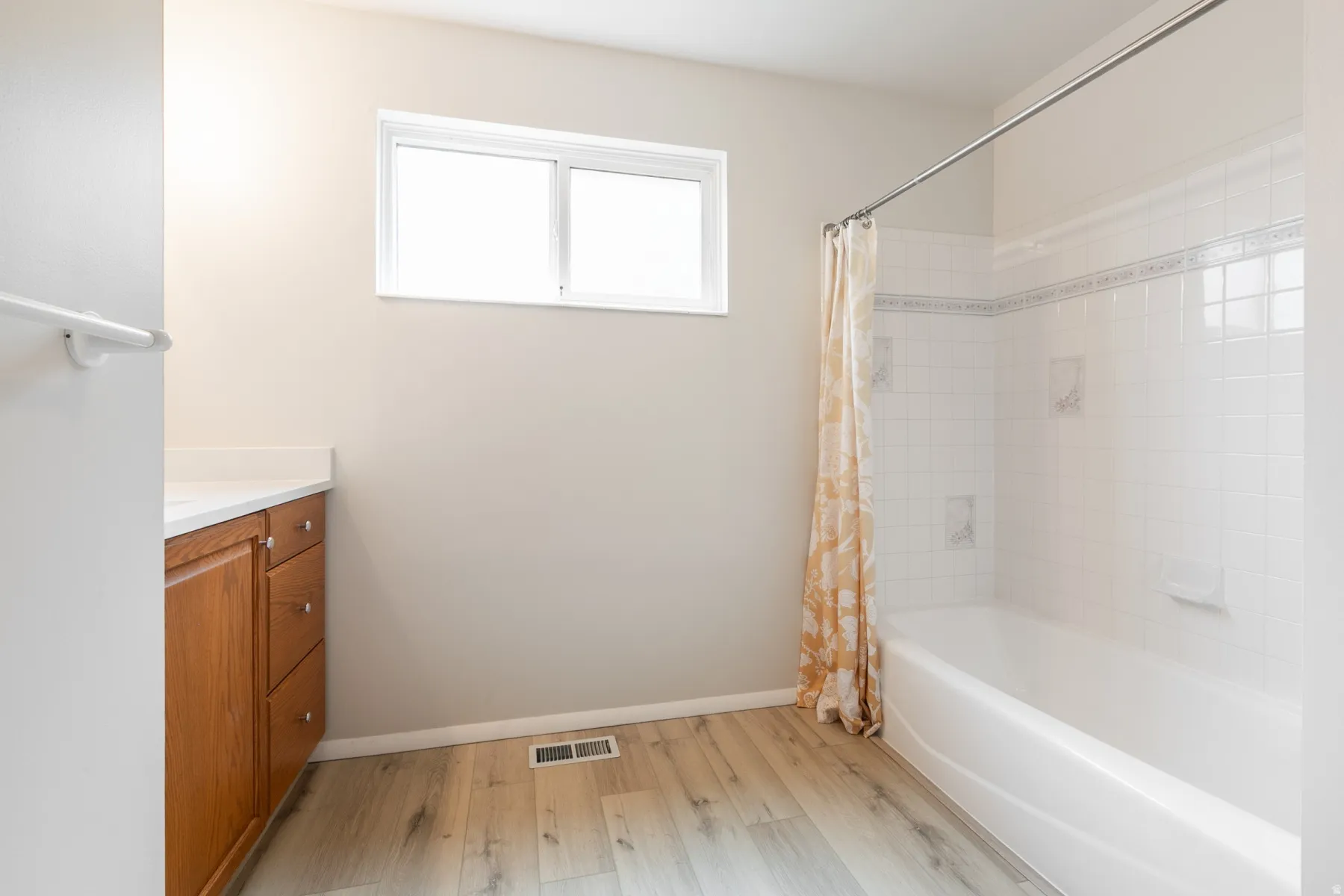 White tile shower/tub combination with an accent border, wood-finish flooring, and a window