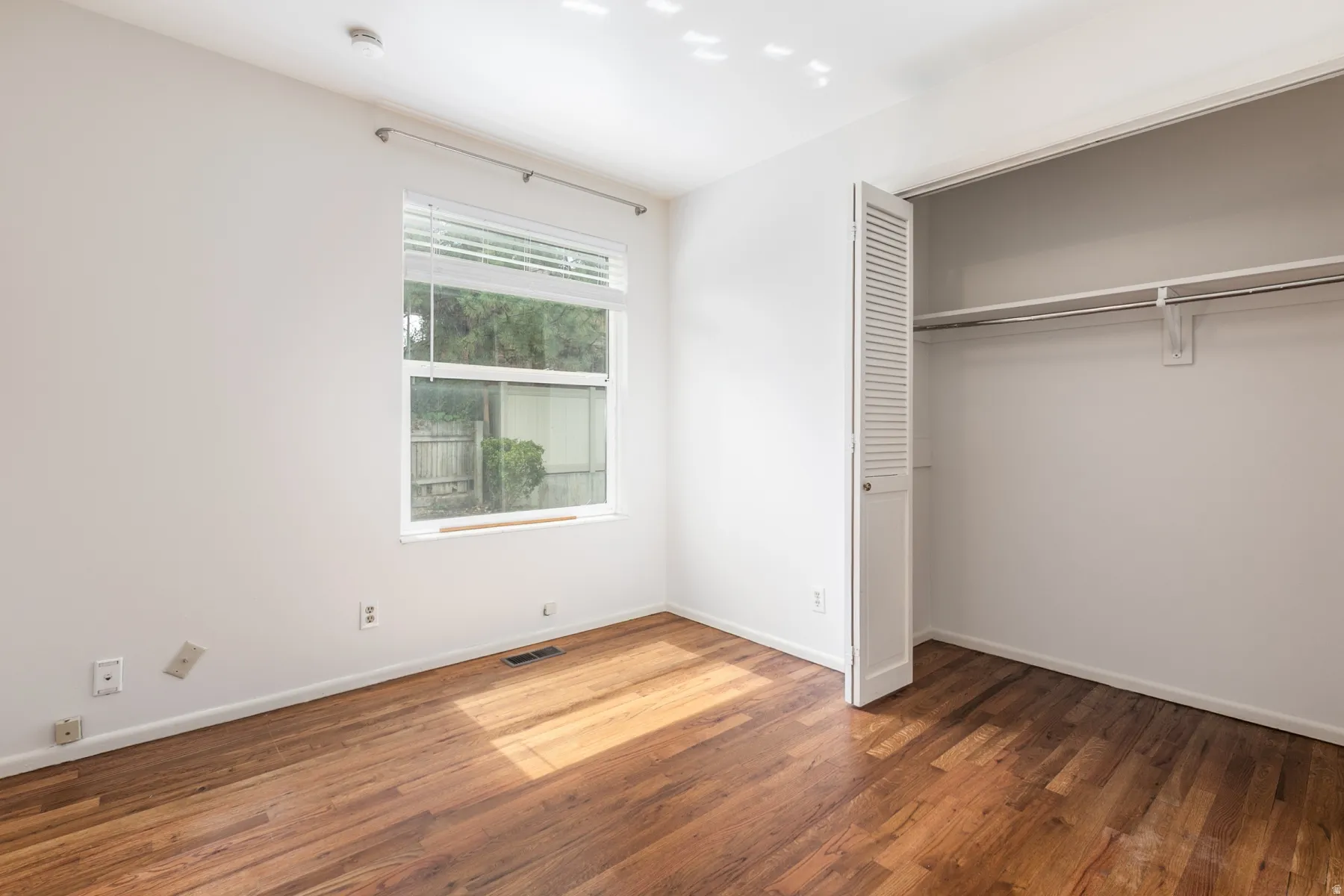 Hardwood flooring, single window with blinds, bi-fold louvered closet doors, and built-in closet shelving