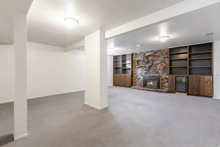 Stone-clad fireplace with black metal insert, built-in shelving, wood-finish cabinetry, and recessed lighting