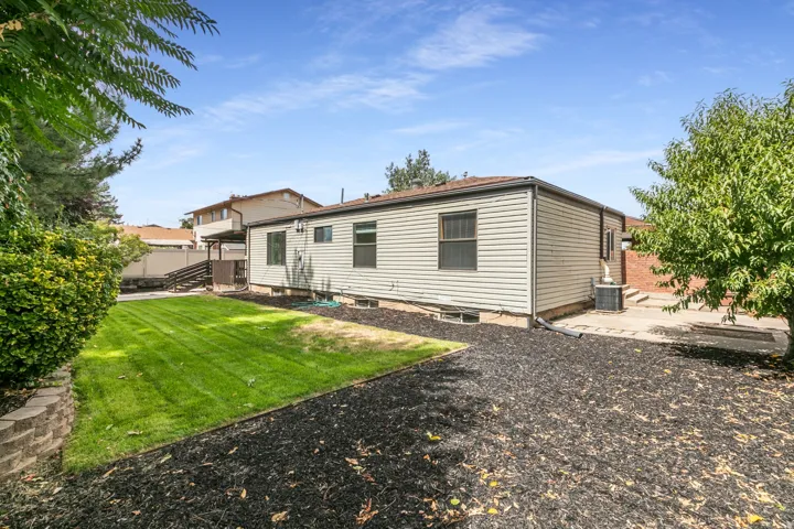 Expansive backyard featuring a manicured lawn, established landscaping, bark ground cover, and a concrete patio