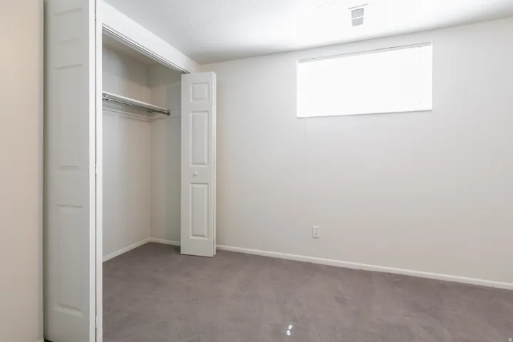 Room featuring a window, gray carpeting, and a bi-fold door closet with a hanging rod