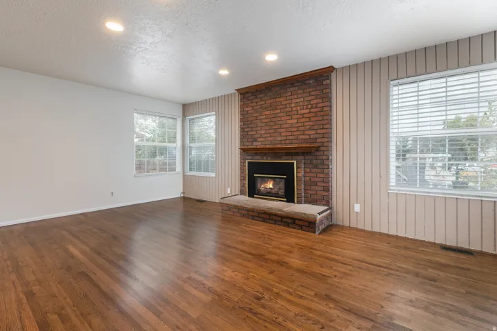 Spacious living area featuring rich wood-finish flooring, recessed ceiling lighting, and abundant natural light from multiple large windows