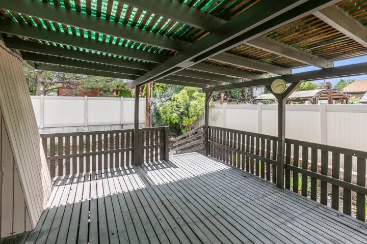 Expansive wood deck with a slatted privacy railing, covered by a slatted pergola roof with translucent green panels