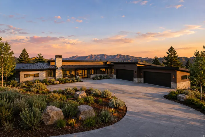 Contemporary architecture with stone and wood siding, multiple garage doors, extensive front landscaping, and a concrete driveway