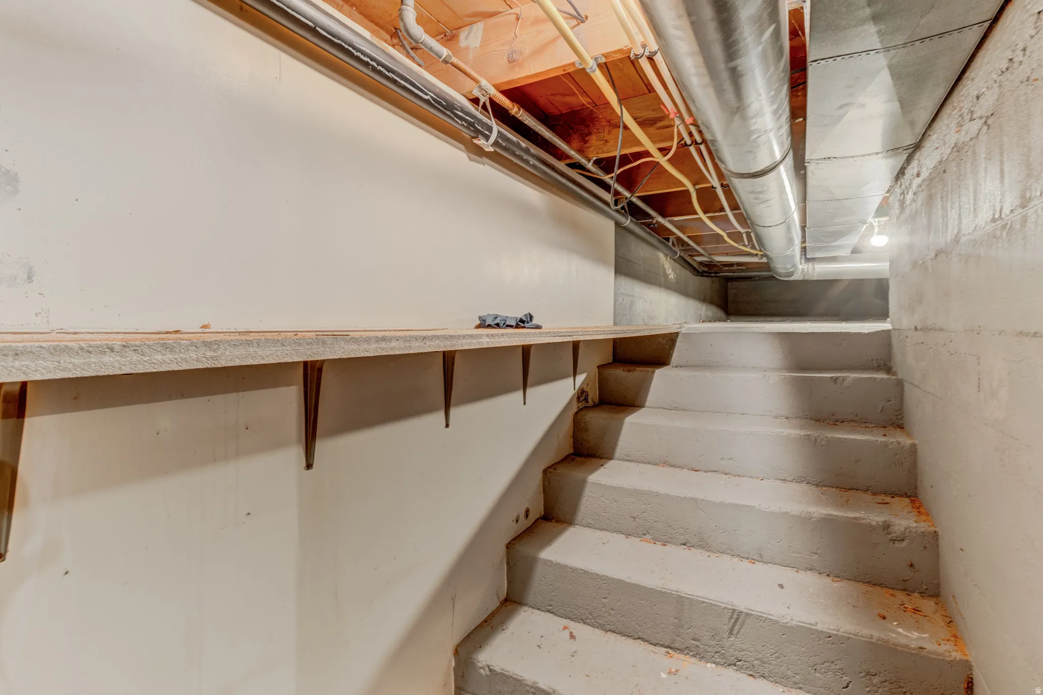 Concrete stairwell leading to a lower level, featuring exposed overhead piping and ductwork