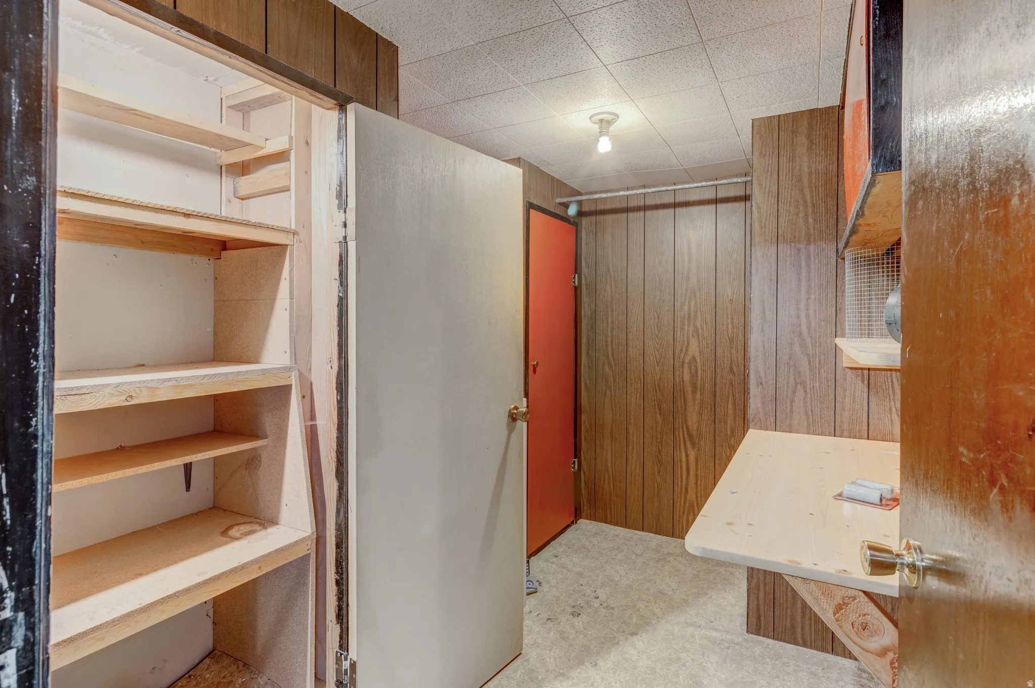 Built-in shelving, wood-paneled walls, a drop ceiling, a surface-mounted light fixture, and a red door