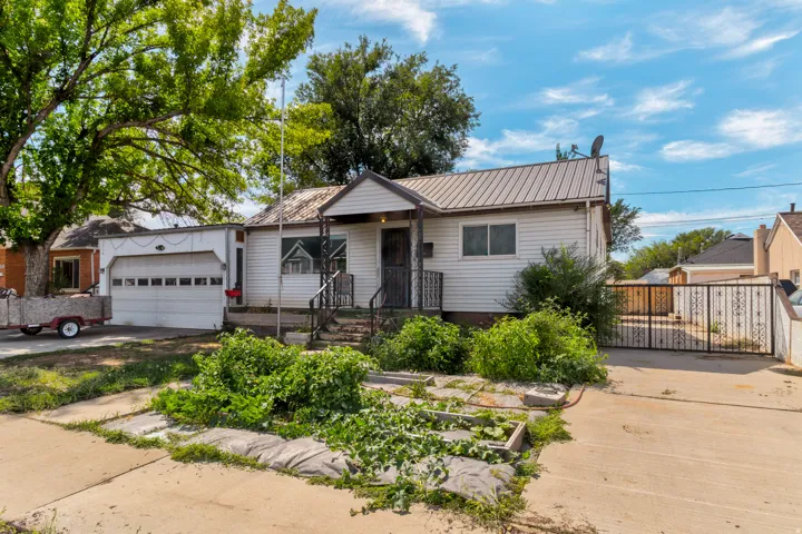 Single-story exterior with white siding, metal roof, covered porch, and attached garage