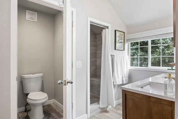 Bathroom featuring a wood-finish vanity with an integrated sink, a large window, a shower with a tiled surround, and wood-finish flooring