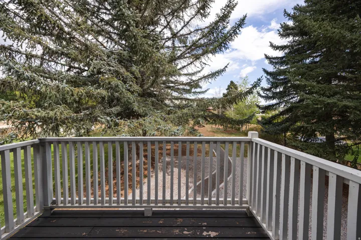 Balcony featuring a wooden railing, dark-stained wood flooring, and surrounding mature trees