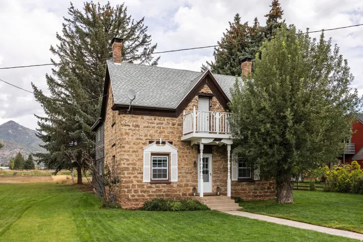Stone exterior construction with a textured shingle roof, white balcony, and front entry path