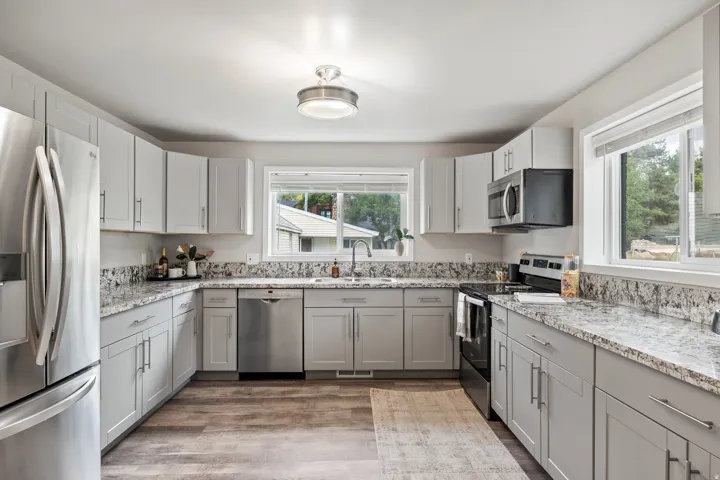 U-shaped kitchen featuring wood-finish flooring, light gray cabinetry, light-toned countertops, stainless steel appliances, and a window above the sink