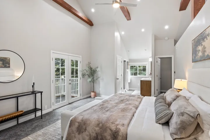 Vaulted ceilings with exposed wood beams, white double French doors, recessed lighting, and an attached bathroom with a wood-finish vanity