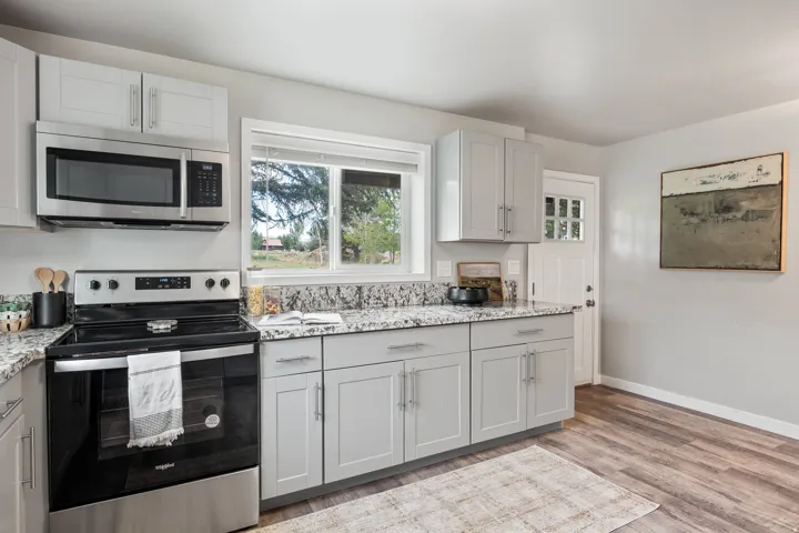 Kitchen featuring light gray cabinetry, stainless steel appliances, granite countertops, and wood-finish flooring