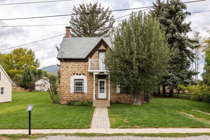 Stone exterior residence featuring a front balcony, an asphalt shingle roof, and a red brick chimney