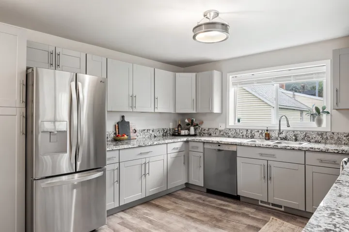 Light gray cabinetry with brushed nickel hardware, granite countertops, stainless steel appliances, wood-finish flooring, and an undermount double-basin sink