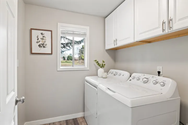 White upper cabinetry with brushed nickel hardware, wood-finish flooring, and a window with white trim