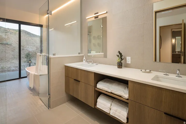 Modern bathroom featuring a freestanding soaking tub, a seamless glass shower enclosure, a dual vanity with undermount sinks, and integrated wood-finish cabinetry