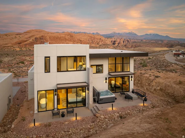 Modern facade featuring large windows, a built-in outdoor spa, a stone patio, and panoramic mountain scenery