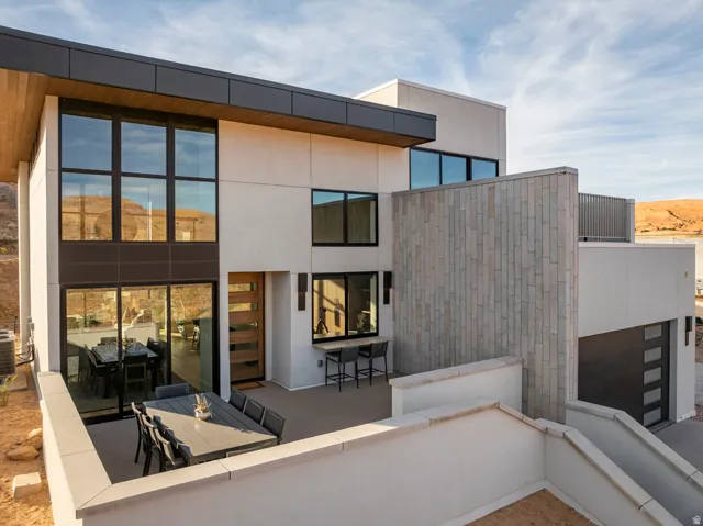 Contemporary exterior showcasing clean lines, an expansive outdoor patio, multi-panel wood entry door, a dark garage door, and a textured stone facade accent