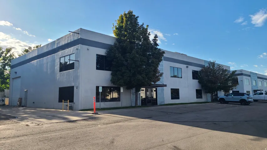 Two-story commercial building with a light gray stucco exterior and a dark gray accent band, featuring multiple large windows and a prominent garage door