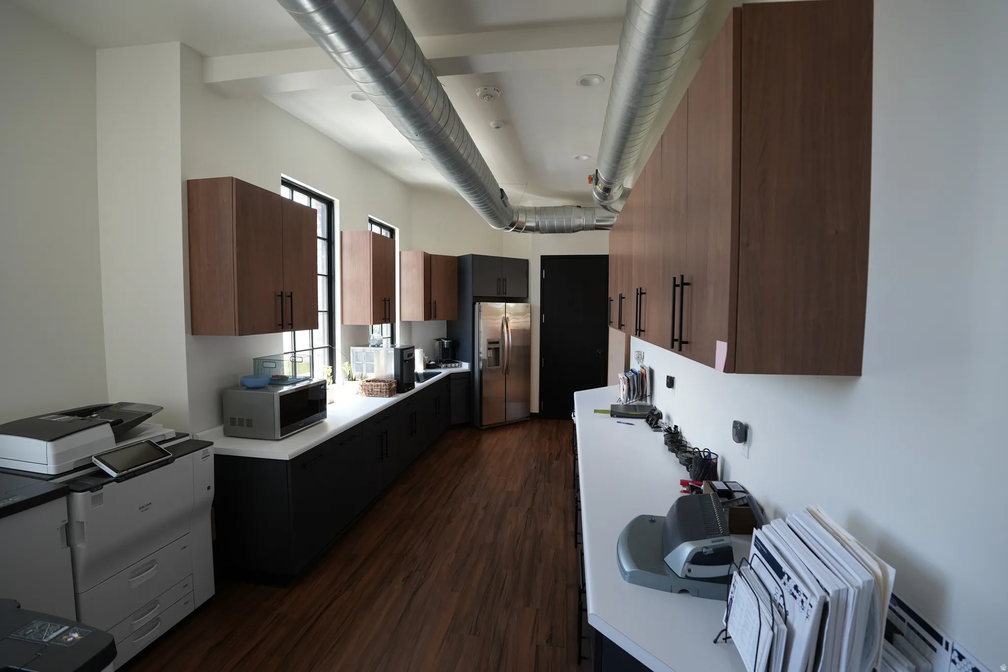 Wood-finish flooring, exposed ductwork, white walls, and dark cabinetry with light countertops
