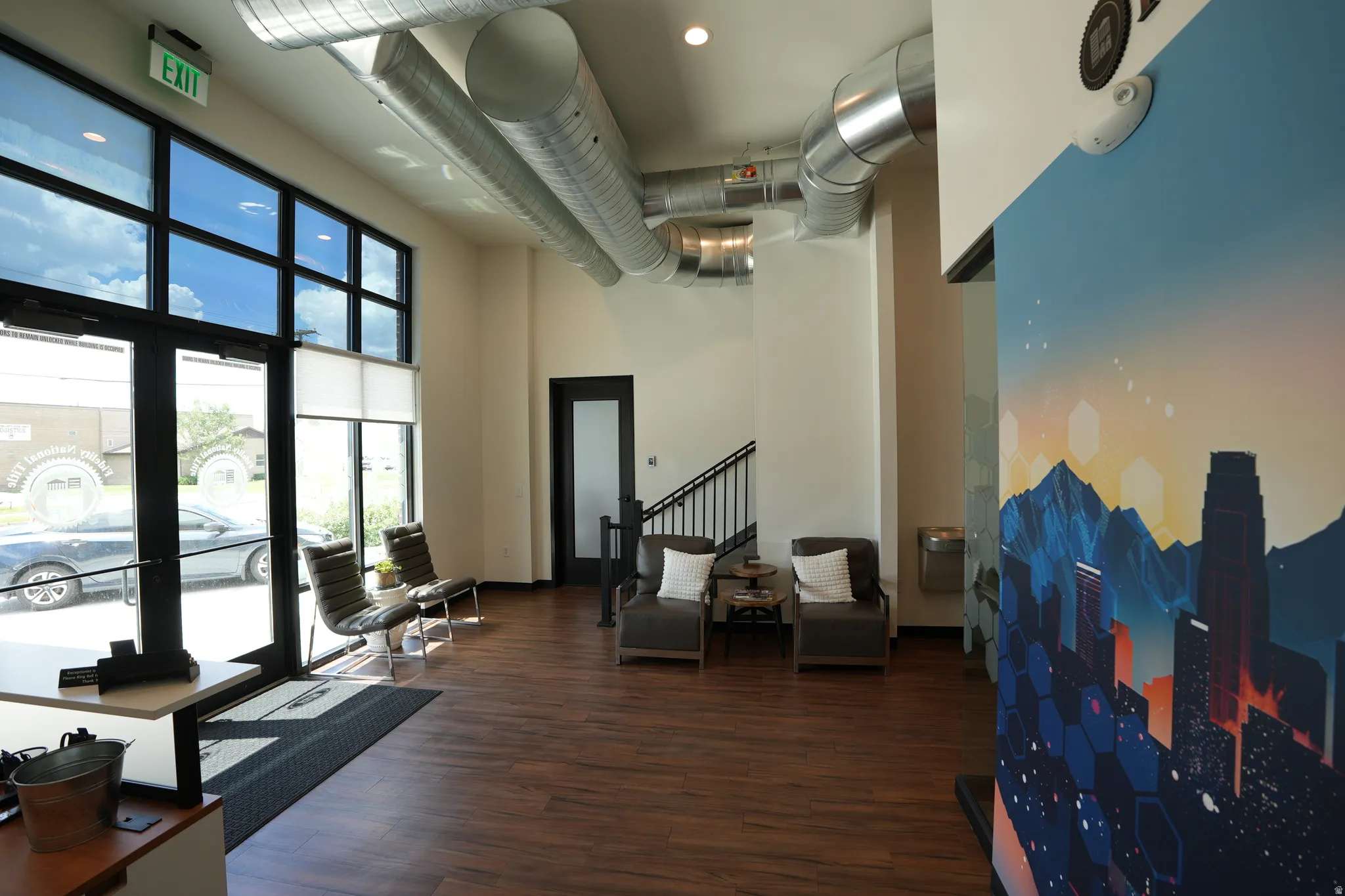 Wood-finish flooring, high ceilings with exposed ductwork, and a wall of windows featuring transom lites