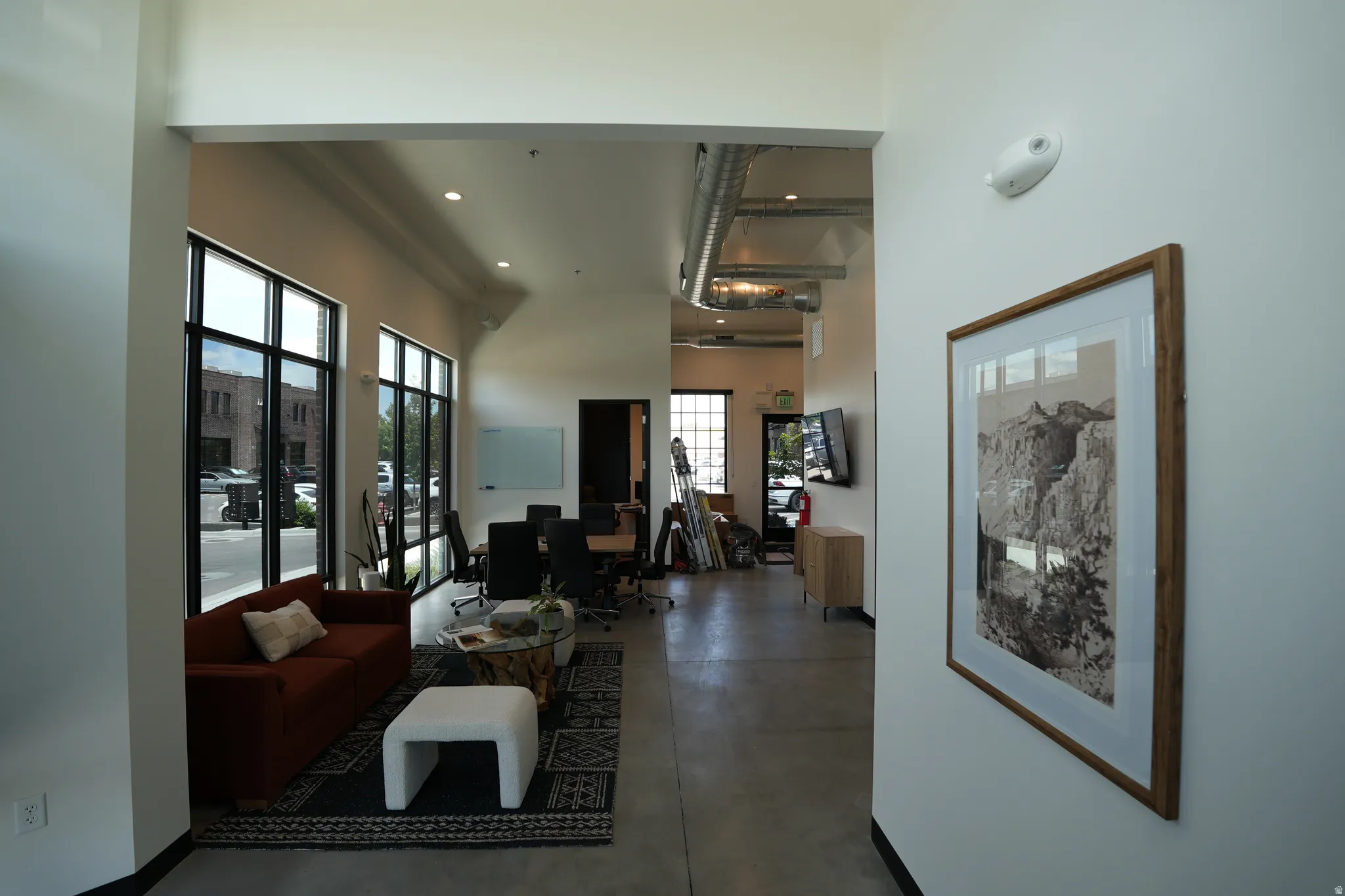 Expansive interior featuring multiple large windows with black frames, exposed industrial ductwork, recessed lighting, and light-toned walls