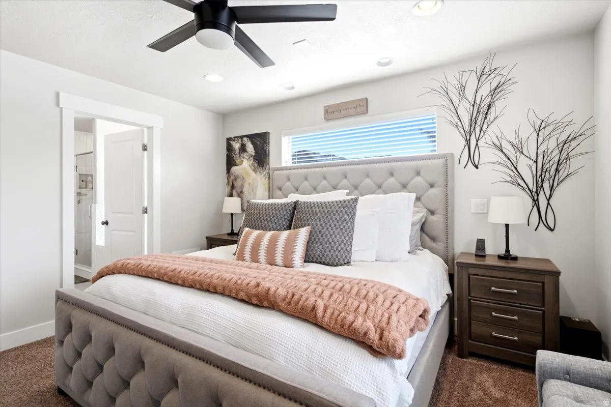 Primary Bedroom featuring a tufted upholstered headboard, recessed ceiling lighting, ceiling fan with integrated light fixture, wood-finish nightstands with drawer storage, and large window with horizontal blinds and transom detailing