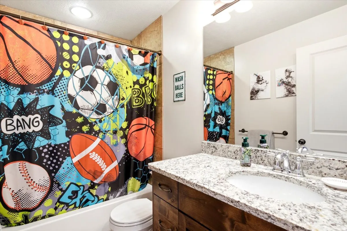 Bathroom featuring a white porcelain tub, toilet, wood-finish vanity with an integrated sink, polished chrome faucet, and a large wall-mounted mirror