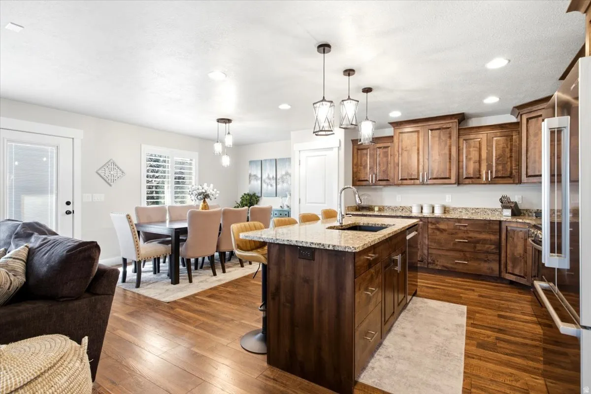 Kitchen with wood cabinetry, granite countertops, an island with a sink, stainless steel appliances, and recessed lighting