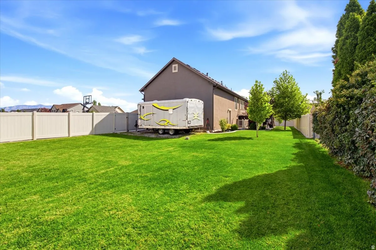 Expansive backyard featuring a manicured lawn, full privacy fencing, and mature trees