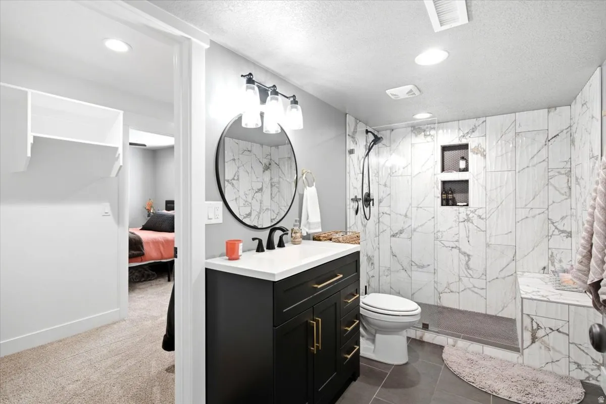 Bathroom featuring a modern black vanity with gold-tone hardware, white countertop, round mirror, and a walk-in shower with tile surround and built-in niches